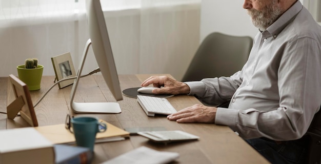 Foto uomo anziano che usa il suo computer a casa