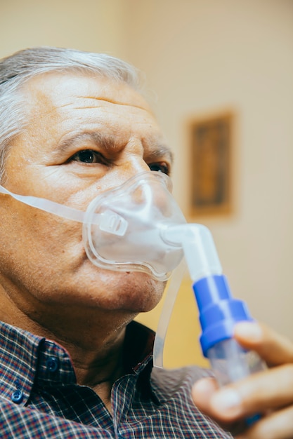 Senior man using medical equipment for inhalation with respiratory mask, nebulizer