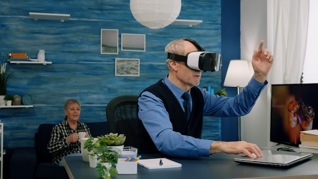 Photo senior man using virtual reality goggles in living room gesturing