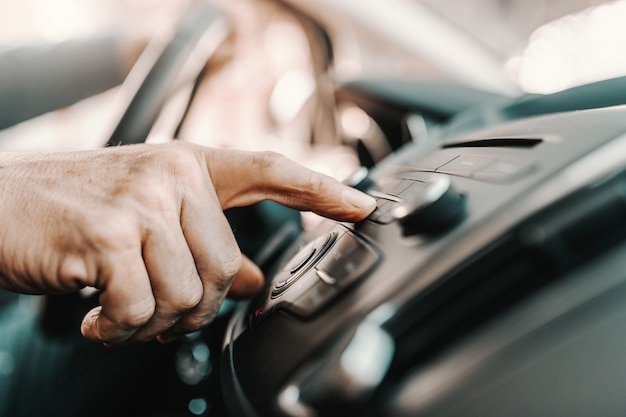 senior man veranderende radiostation zittend in zijn auto.