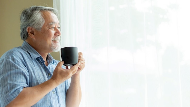 Senior man voelt zich gelukkig als hij 's ochtends koffie drinkt en geniet van de tijd in zijn huis binnenshuis achtergrond levensstijl senior geluk concept