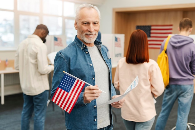 Foto uomo anziano votante con la bandiera americana che guarda la telecamera in fila per votare al seggio elettorale