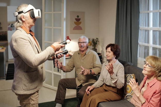 Senior man in vr headset holding gamepads while controlling picture on screen