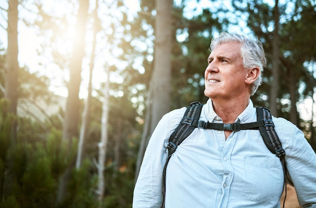 Senior man walking on hike in nature looking at view on mountain and hiking on a relaxing getaway vacation alone in the countryside Retired mature and happy guy on walk for exercise and fitness