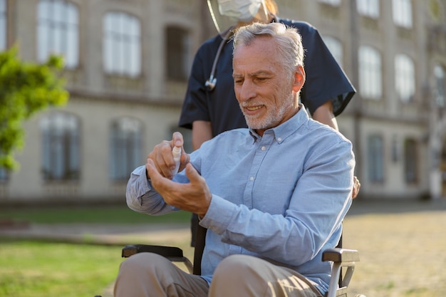 Photo senior man in wheelchair cleaning his hands with antibacterial sanitizer as a hygiene measure to