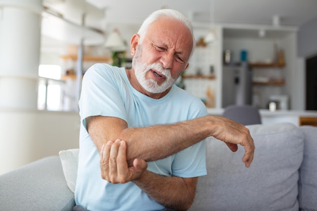 Photo senior man with arm painold male massaging painful hand indoors old man hand holding his elbow suffering from elbow pain senior man suffering from pain in hand at home old age health