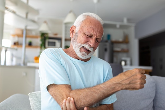 Senior man with arm painOld male massaging painful hand indoors Old man hand holding his elbow suffering from elbow pain Senior man suffering from pain in hand at home Old age health