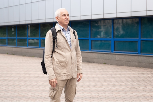 Senior man with backpack outdoors in city landscape near office buildings