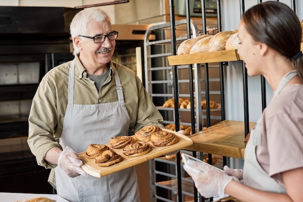写真 パン屋で働くパンとタブレットを持つ彼の娘を持つ年配の男性