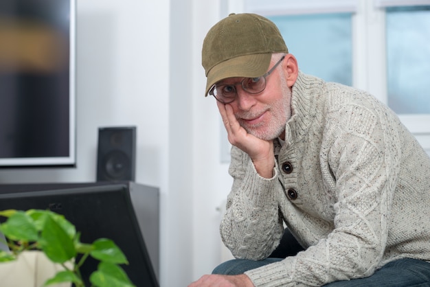 Senior man with cap using laptop at home