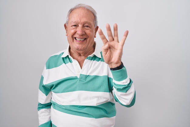 Senior man with grey hair standing over white background showing and pointing up with fingers number four while smiling confident and happy