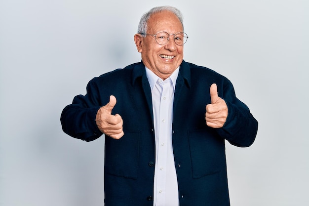 Uomo anziano con i capelli grigi che indossa uno stile casual e segno di successo degli occhiali facendo un gesto positivo con la mano, pollice in alto sorridente e felice. espressione allegra e gesto vincente.