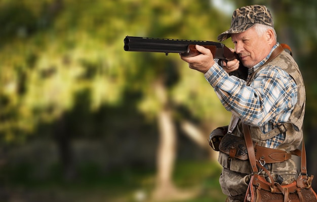 Senior man with gun in green forest