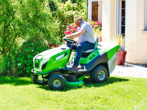 Senior man with hat on tractor gardening cutting grass in summer