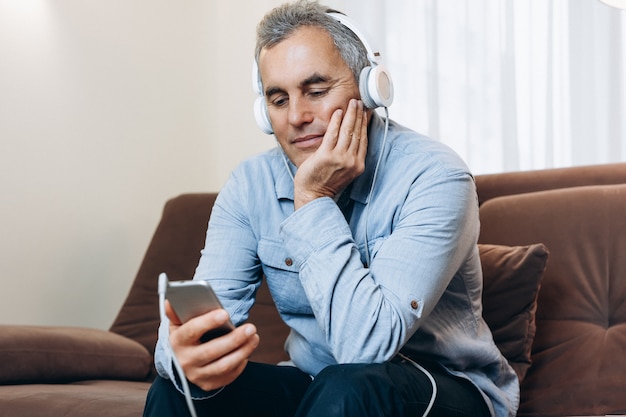 Senior man with headphones is watching an interesting movie from his phone