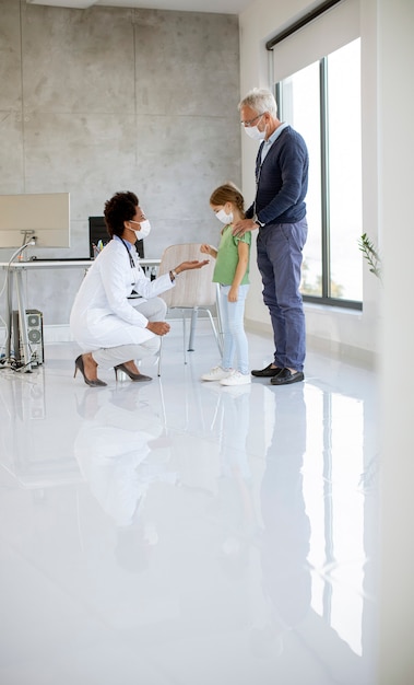 Senior man with his little grandaughter at the pediatrician examination by African american female doctor