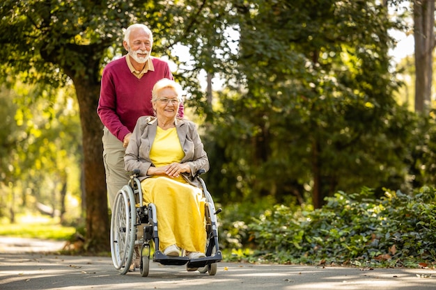 Photo senior man with his wife in wheelchair going for a walk in public park