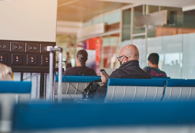 Foto uomo anziano con dispositivi di ricarica per smartphone nella sala dell'aeroporto con carrello a mano per bagagli