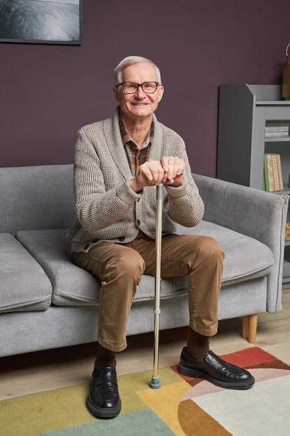 Senior man with stick sitting on sofa