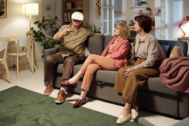 Senior man with vr headset sitting on couch next to two aged women