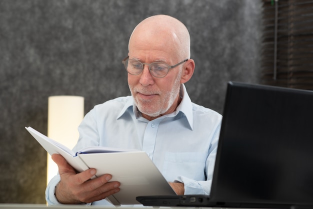 Senior man with white hairs and glasses reading book