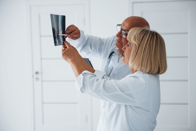 Старшие врачи мужчины и женщины в белой форме исследуют рентген человеческих ног.