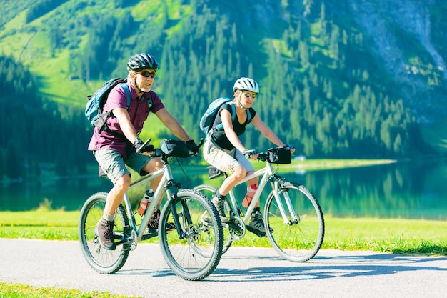 Foto uomo e donna anziani in bicicletta per strada vicino al lago