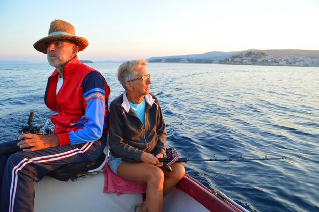 Photo senior man and woman sitting on boat in river against sky