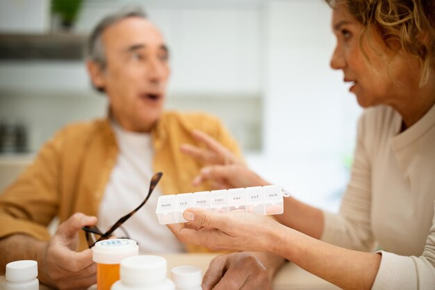 Senior man and woman taking medicine in morning wife giving daily pills to her husband kitchen