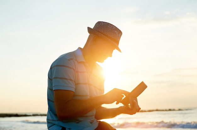 Senior man working on his smartphone on the beach during sunset