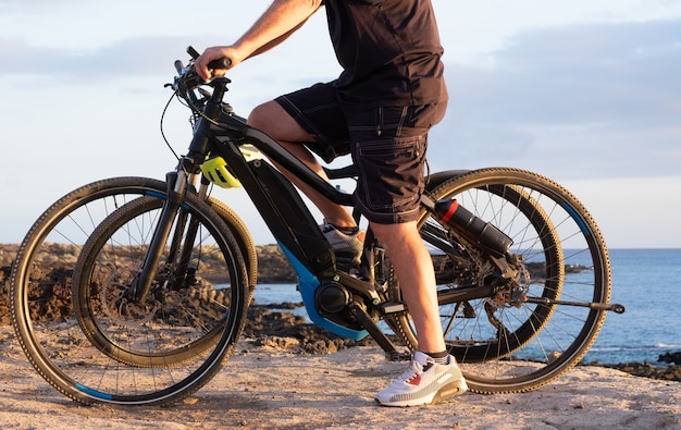 Senior man zijn bici rijden op de kliffen. Horizon over zee bij zonsondergang licht. Twee elektrische fietsen met accu en motor. Eén volk in activiteit