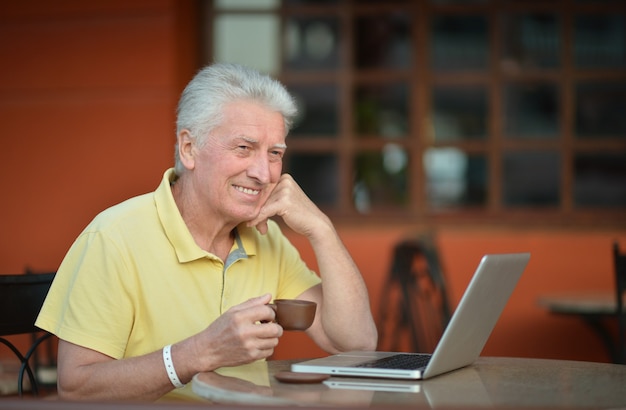 Senior man zit met laptop en koffie in hotel