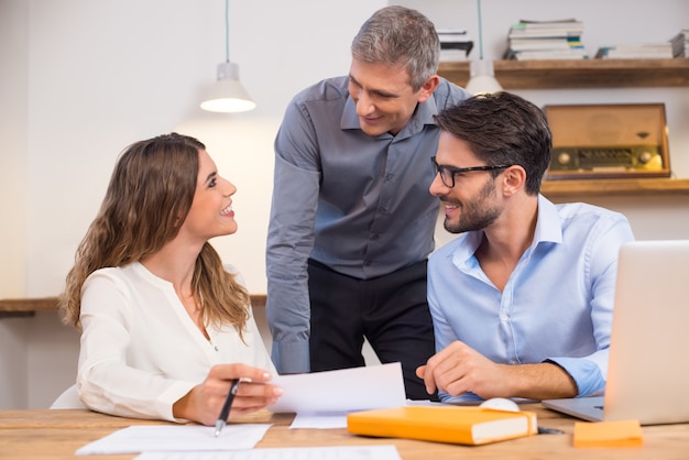 Senior manager che interagisce con i nuovi tirocinanti in ufficio. giovani dipendenti sorridenti in una conversazione con il dirigente in ufficio. lavoro di squadra felice di affari che sorride nell'ufficio con il leader.