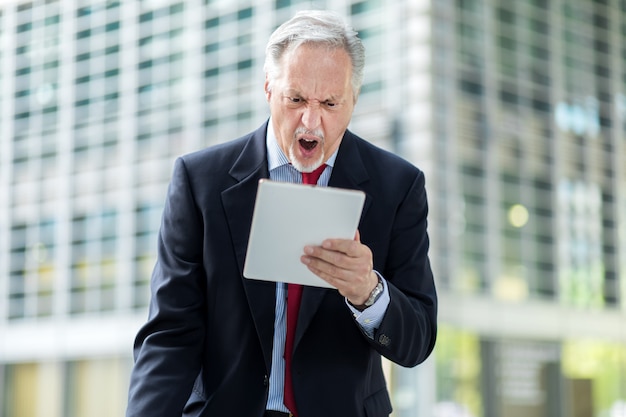 Senior manager looking anrgy because he reads bad news on his tablet