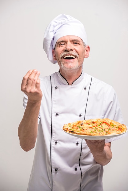 Senior mannelijke chef-kok in uniform houden pizza.