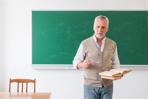 Senior mannelijke professor bedrijf boeken en glazen tegen schoolbord