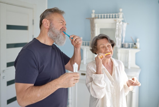 Foto coppia sposata anziana che si lava i denti insieme in piedi in casa bagno mattina o sera routine quotidiana di igiene della famiglia anziana