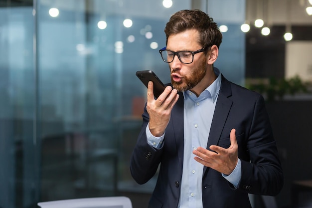 近くのオフィス内のビジネス スーツの電話ビジネスマンで話しているシニアの成熟した上司の怒っている叫び