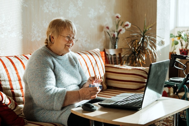 Senior mature candid real caucasian woman look at laptop screen at home and hold gift box happy