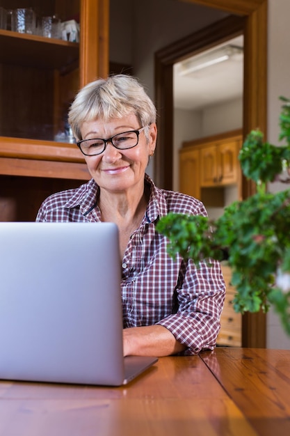 Senior mature woman using laptop at home watching online webinar