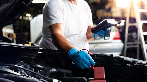 Senior mechanic man uses multimeter voltmeter to check voltage level in car battery at car service and maintenance garage