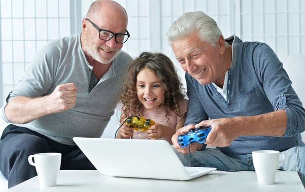 Senior men and granddaughter having fun and playing on laptop  at home