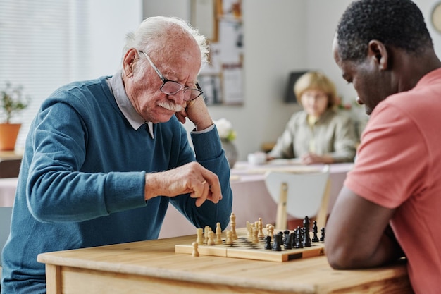 Senior men spending their leisure time to play chess together at table in nursing home