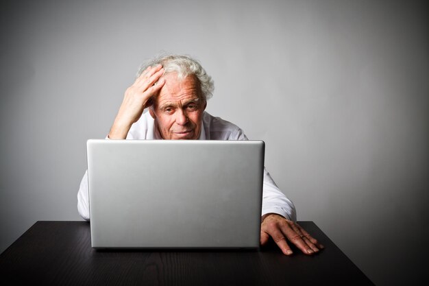 Senior men with head in hands using laptop while sitting against wall