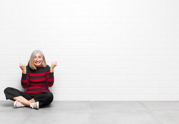 Donna graziosa di mezza età o senior che grida trionfante, ridendo e sentendosi felice ed eccitata mentre celebra il successo