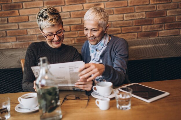 Senior moeder zit in café-bar of restaurant met haar dochter van middelbare leeftijd, ze lezen kranten en genieten van een gesprek.