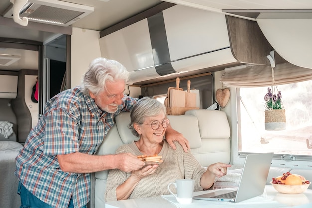 Senior mooi stel in reisvakantie in een camper die op laptop bladert terwijl u samen geniet van het ontbijt