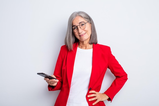 Senior mooie vrouw die gelukkig lacht met een hand op de heup en zelfverzekerd... zakelijk en telefoonconcept