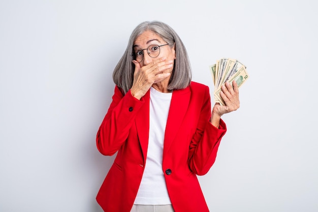 Senior mooie vrouw die mond bedekt met handen met een geschokt. bedrijfs- en bankbiljettenconcept