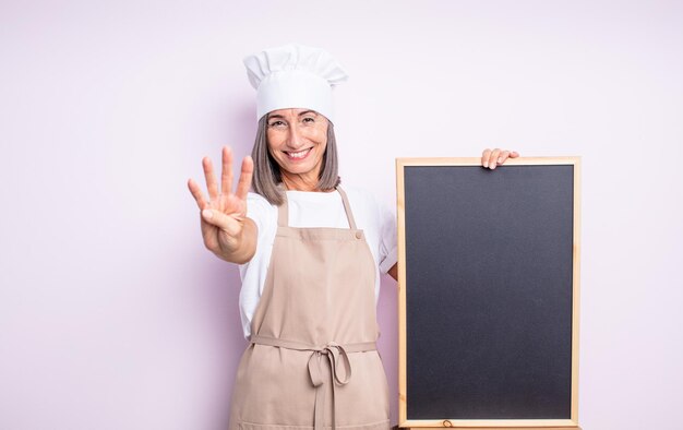 Senior mooie vrouw lacht en ziet er vriendelijk uit, met nummer vier. chef-kok en schoolbordconcept